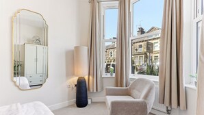 A hotel room with a bed, a chair, a lamp, a mirror, and a window with curtains. - Beautiful central Harrogate Flat (North Yorkshire)