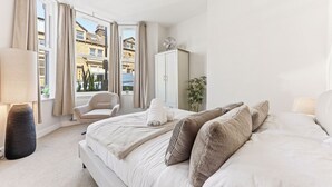 A bedroom with a large bed, a chair, a wardrobe, and a window with curtains. - Beautiful central Harrogate Flat (North Yorkshire)