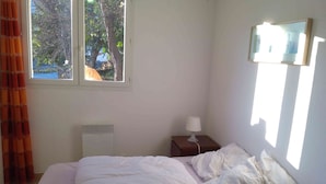 Een slaapkamer met een bed, een nachtkastje met een lamp, een raam en een radiator.