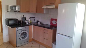Een kleine keuken met houten kastjes, een magnetron, een wasmachine, een Samsung koelkast en een koffiezetapparaat.