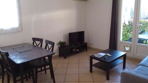Een woonkamer met een eettafel, stoelen, een bank, een televisie en een raam met gordijnen.
