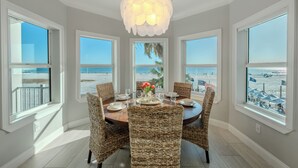 Un coin repas avec vue sur la plage, des chaises en osier, un lustre et une table dressée pour quatre personnes.