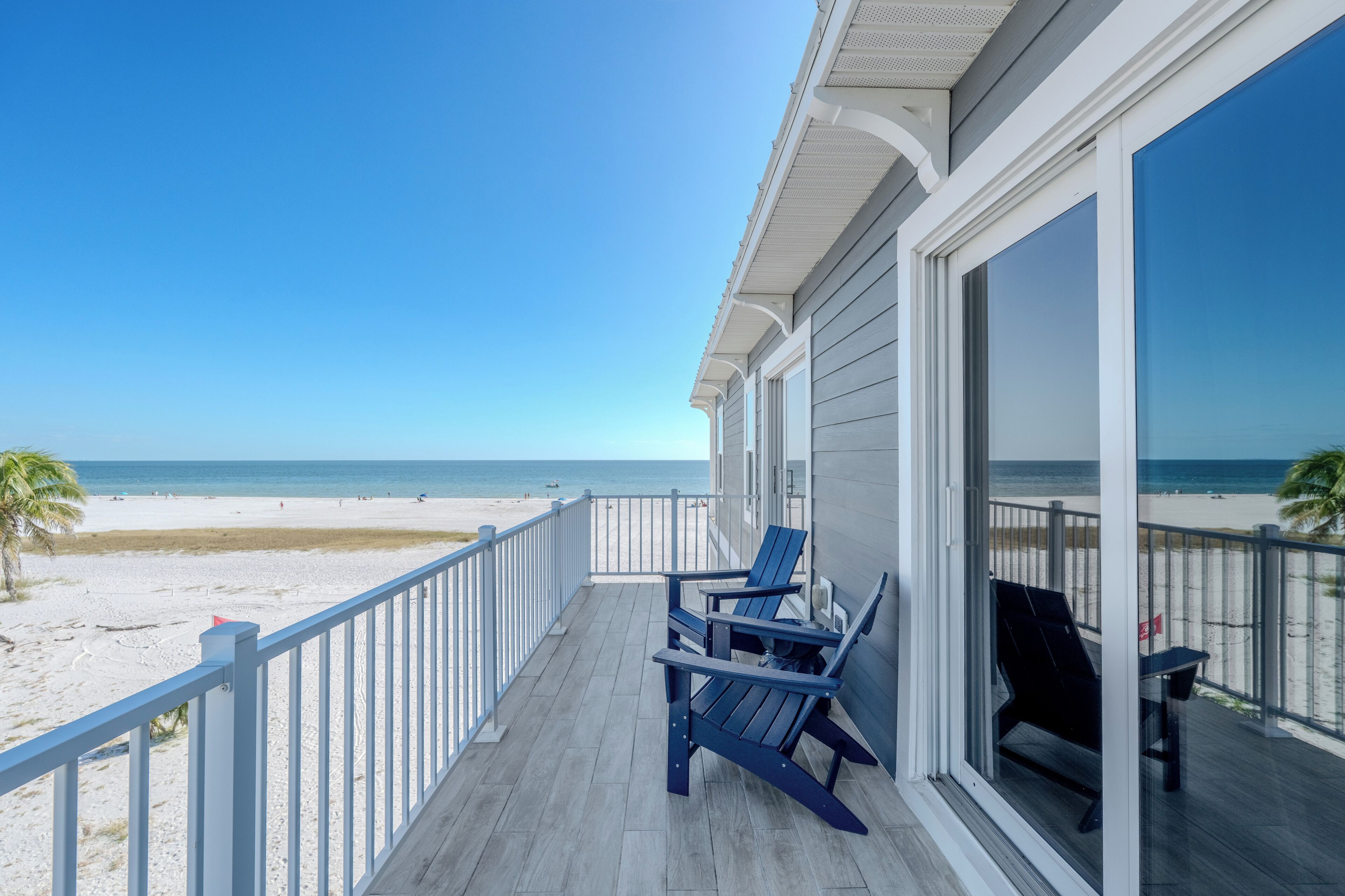 Ein Balkon mit zwei Adirondack-Stühlen mit Blick auf einen Strand.