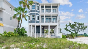 Une propriété en bord de mer, composée de plusieurs étages, dot ée de balcons, d’un porche couvert et d’une plage de sable en contrebas.