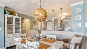 A dining area with a white table, white chairs, and a wicker chair. - Captain's Quarters: Soundfront | Private Boat Slip (Manteo)