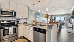 A modern kitchen with white cabinets, stainless steel appliances, a granite countertop, and pendant lighting. - Captain's Quarters: Soundfront | Private Boat Slip (Manteo)