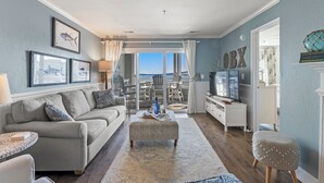 A living room with a sofa, ottoman, and a view to the outside. - Captain's Quarters: Soundfront | Private Boat Slip (Manteo)
