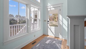 A room with large windows, a door leading outside, and a patterned rug on the floor. - Sea Sounds -  steps to beach access, sleeps 17 and golf cart included (Fripp Island)