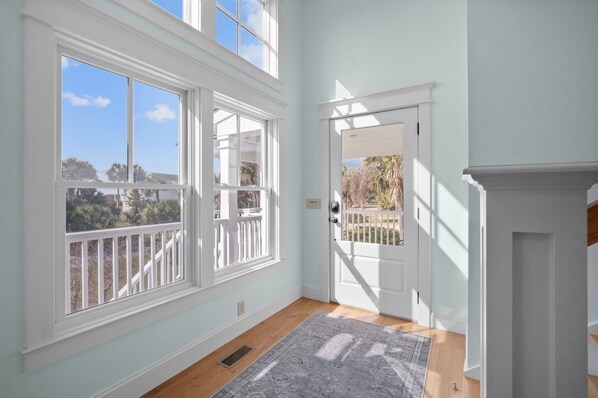 A room with large windows, a door leading outside, and a patterned rug on the floor. - Sea Sounds - steps to beach access, sleeps 17 and golf cart included (Fripp Island)