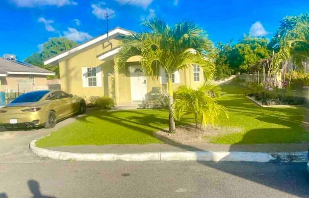 A residential house with a driveway, a parked car, and a well-maintained lawn with palm trees.