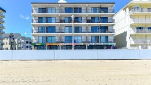 Um hotel com vários andares, varandas, vista para a praia e diversas lojas, incluindo Subway e NY Piercing.
