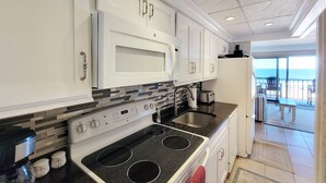 Cozinha moderna com forno embutido, fogão e pia. Janelas amplas oferecem vista para o oceano.