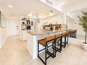 Una cucina con isola centrale, sgabelli da bar e mobili bianchi.
