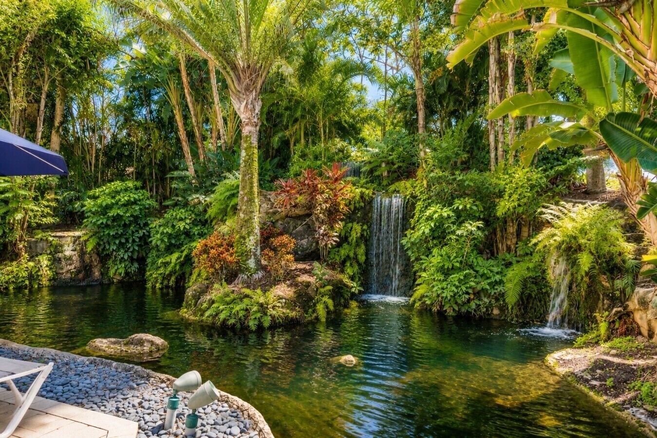A tranquil garden with a pond, a waterfall, and lush vegetation.