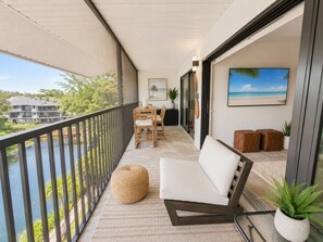 A balcony with a sofa, chairs, and a table, overlooking a body of water and greenery. - Park Shore Resort,Great views-Top Floor BLDGJ#454 (Park Shore Resort)