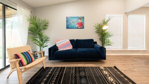 Un salón con un sofá azul oscuro, una silla de madera con un cojín colorido, una alfombra negra estampada y dos plantas en macetas.