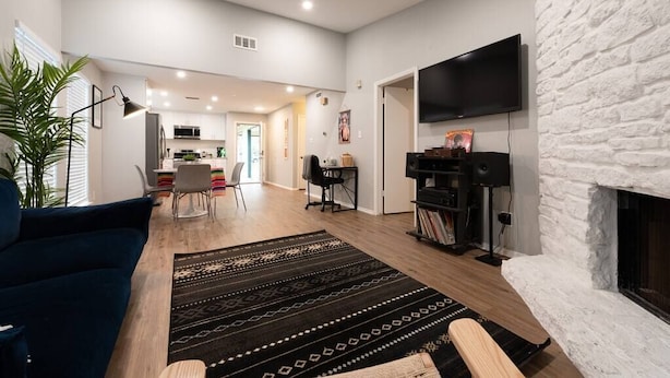 Una sala moderna con chimenea, televisor de pantalla plana montado en una pared de ladrillo blanco, sofá azul oscuro y una mesa de centro de madera.