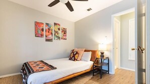 Un dormitorio con cama, ventilador de techo, mesita de noche y decoración en la pared.