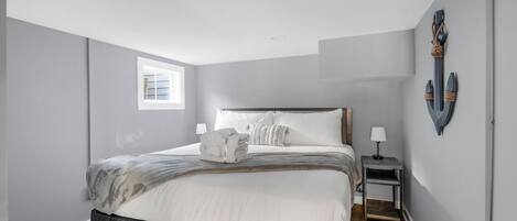 Un dormitorio moderno con una cama grande, una mesita de noche, una pequeña mesa y una ventana.