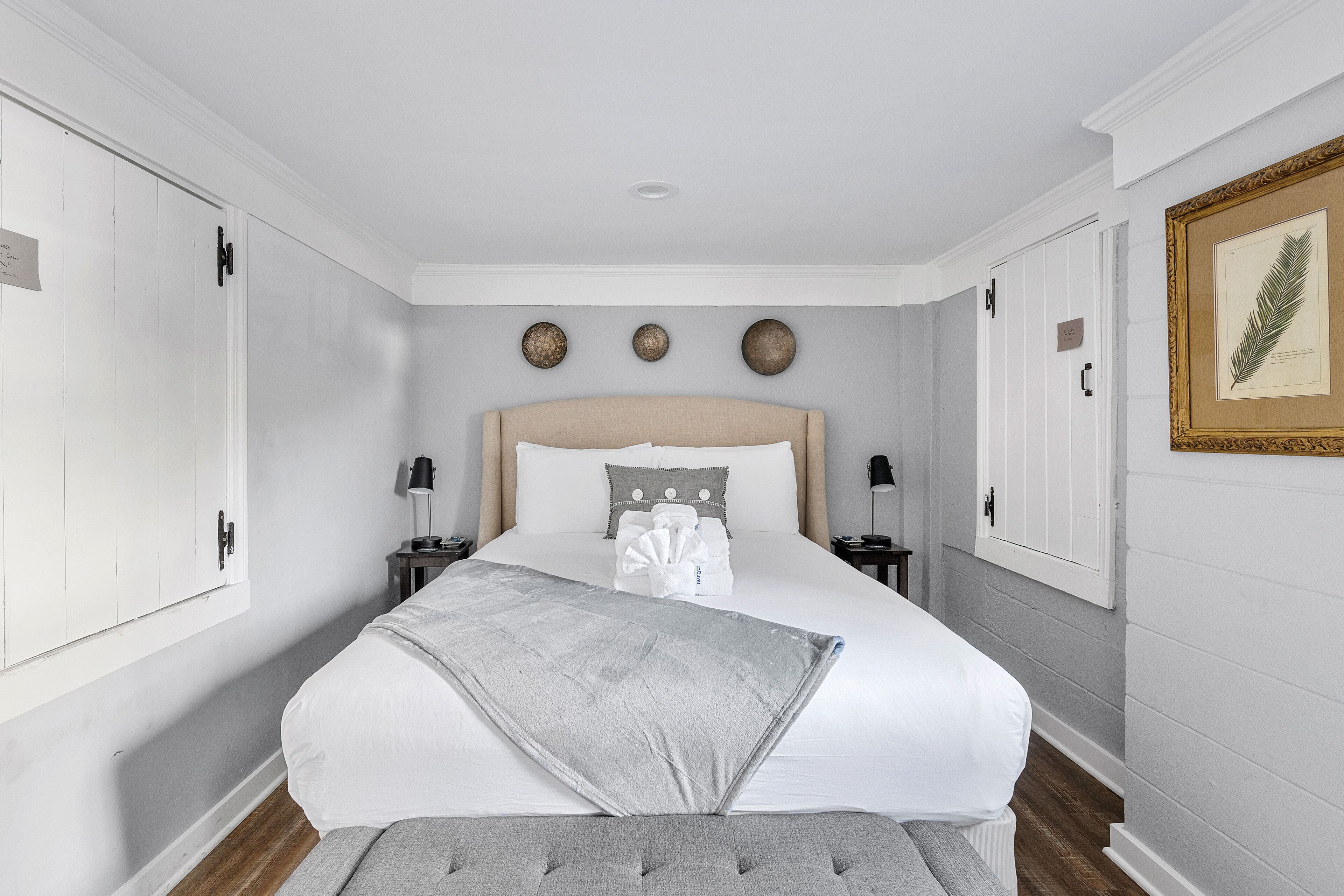 Un dormitorio ordenado con una cama grande, mesitas de noche e impresión enmarcadas de motivos botánicos en la pared.