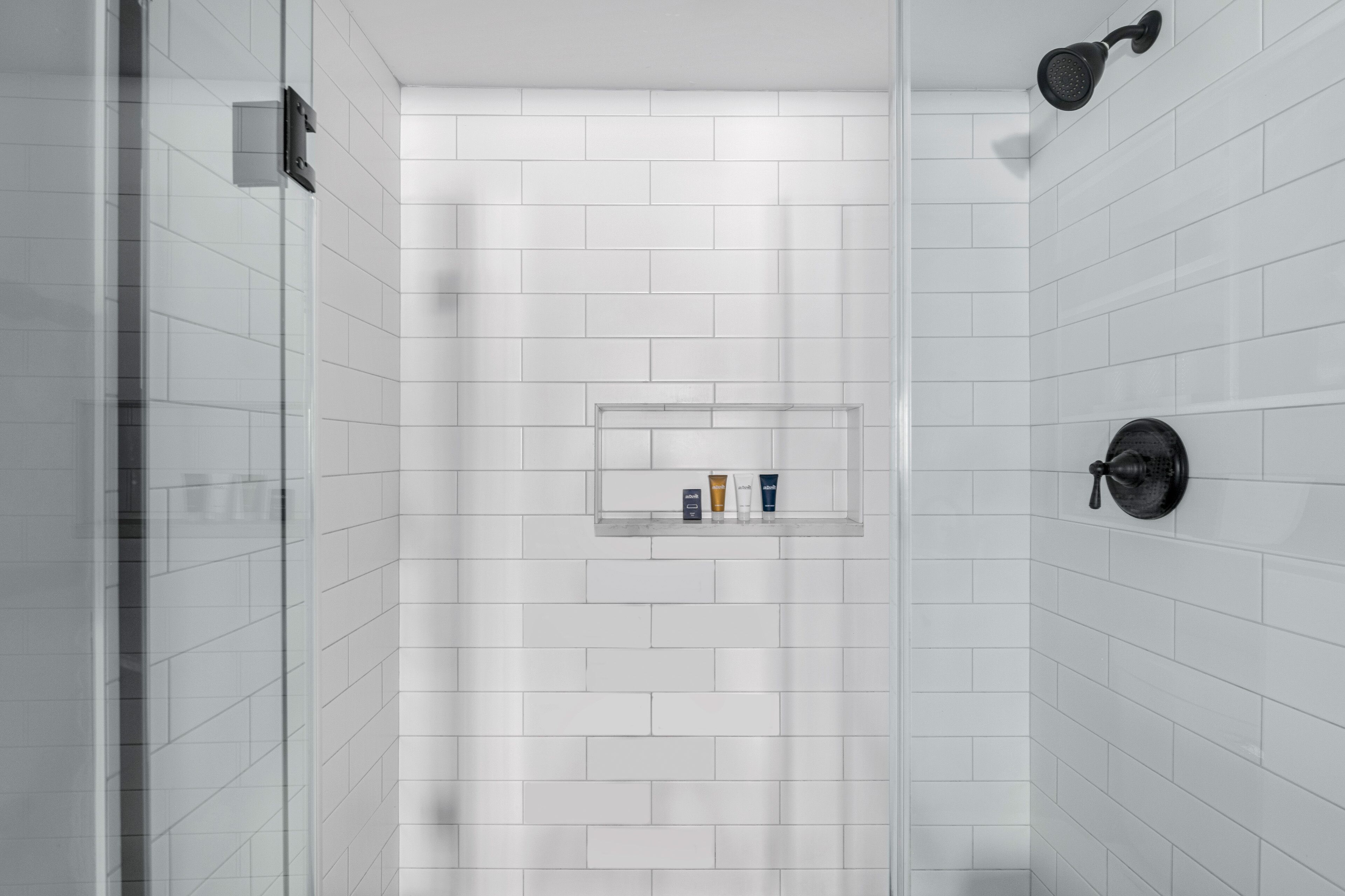 Un baño moderno con azulejos blancos tipo metro, una cabina de ducha de vidrio y un estante empotrado con artículos de aseo.