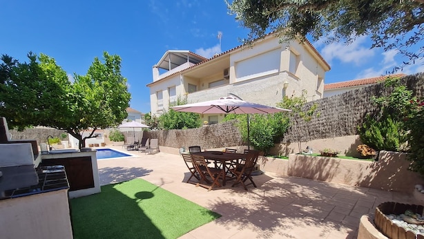 Un jardin avec un barbecue, une table à manger avec des chaises, une piscine et une maison en arrière-plan.