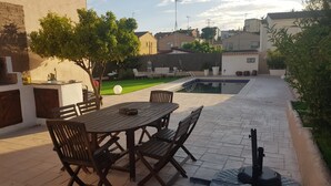 Une terrasse extérieure avec une table et des chaises en bois, une petite piscine et un jardin agrémenté d’arbres et d’une pelouse.