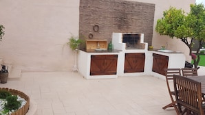 Un espace cuisine extérieur avec un mur en pierre en arrière-plan, un barbecue encastré et des armoires en bois.