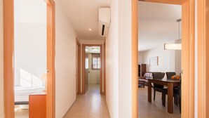 En gang der fører til et spiseområde med et bord og stole, en lampe og en loftmonteret aircondition.