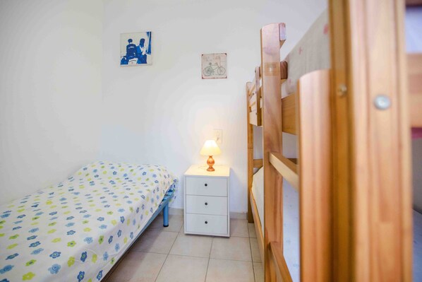 Ein kleines, ordentlich eingerichtetes Schlafzimmer mit einem Einzelbett, einem Nachttisch mit Lampe und einem Holz-Kopfteil.