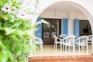 Eine Terrasse mit weißen Stühlen und einem Tisch, blauen Fensterläden und einem gefliesten Boden.