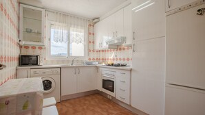 Ett kompakt kök med tvättmaskin, ugn, mikrovågsugn och en liten matplats med ett bord och en bänk.