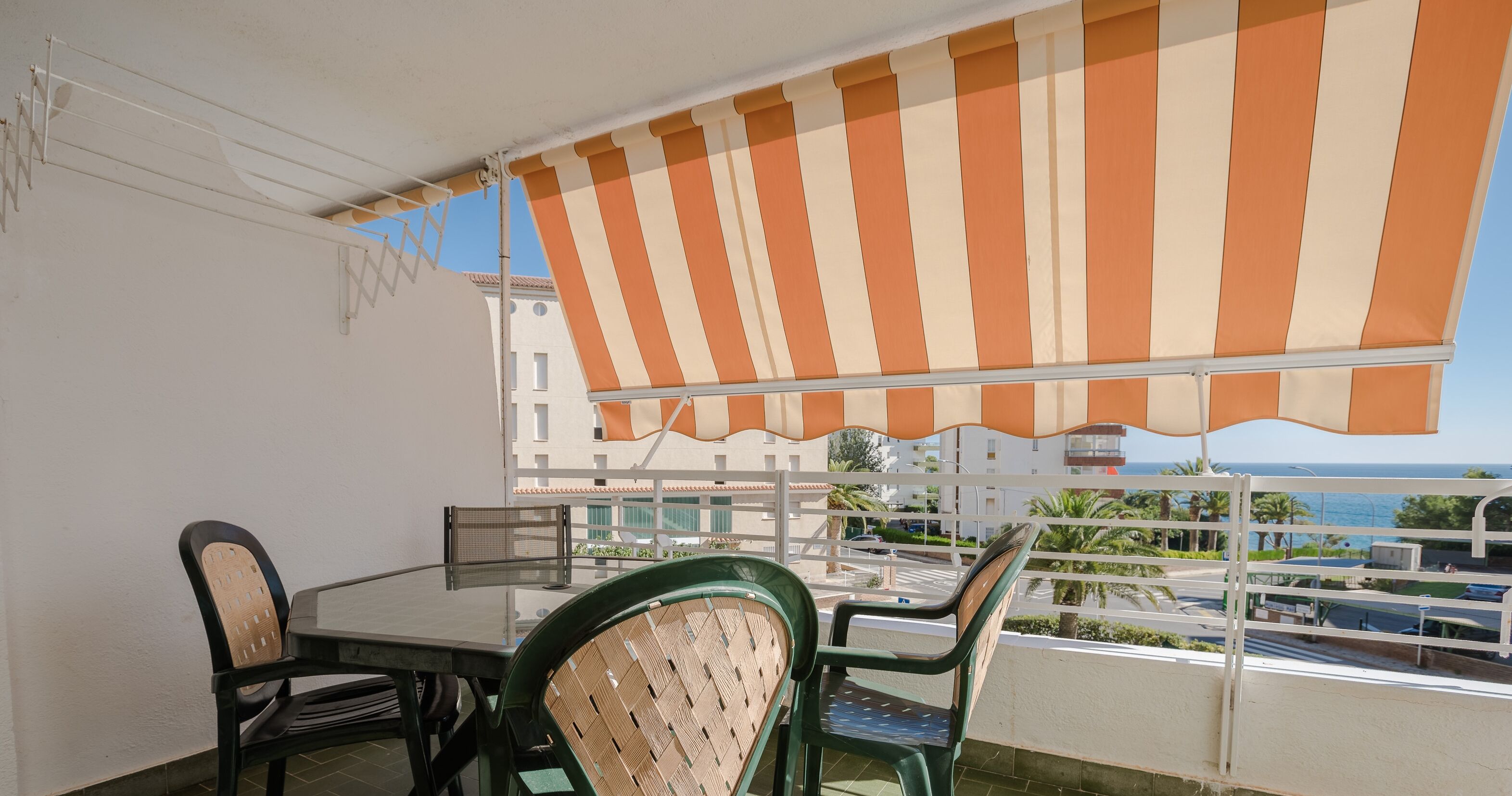 A balcony with a striped awning, a table, and chairs.