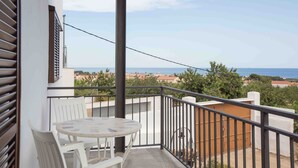A balcony with a table and chairs, a view of the sea, and a wooden fence.