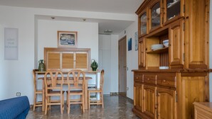 A room with a wooden dining table and chairs, a cabinet with glass doors, and a bed with a blue cover. - Aiguadolç - Alojamientos MarCalma (Tarragona)