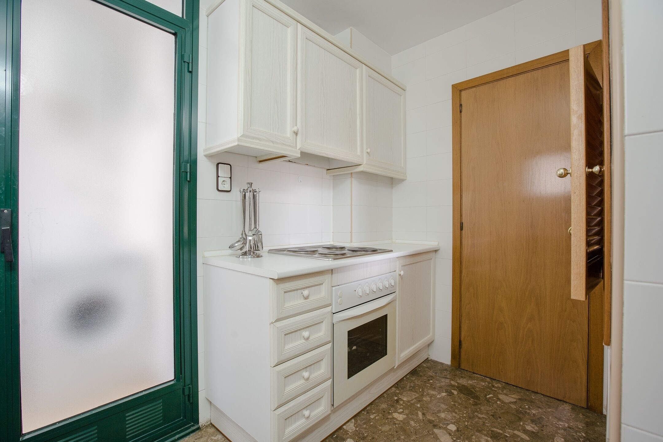 A kitchen with white cabinets, a stove, and a wooden door.