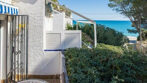 A coastal property with a white exterior, a blue-striped awning, and a view of the sea. - Casa Rosana - Alojamientos Marcalma (Tarragona)
