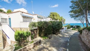 A narrow street lined with white buildings, some with blue shutters, leading to a beach. - Casa Rosana - Alojamientos Marcalma (Tarragona)