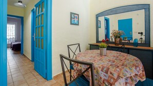 A room with a round table covered with a patterned tablecloth, a blue-framed door, a small potted plant, and a mirror reflecting the door and a blue wall. - Casa Rosana - Alojamientos Marcalma (Tarragona)