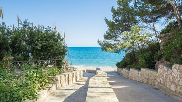 A stone pathway leading to a beach with clear blue water. - Casa Rosana - Alojamientos Marcalma (Tarragona)