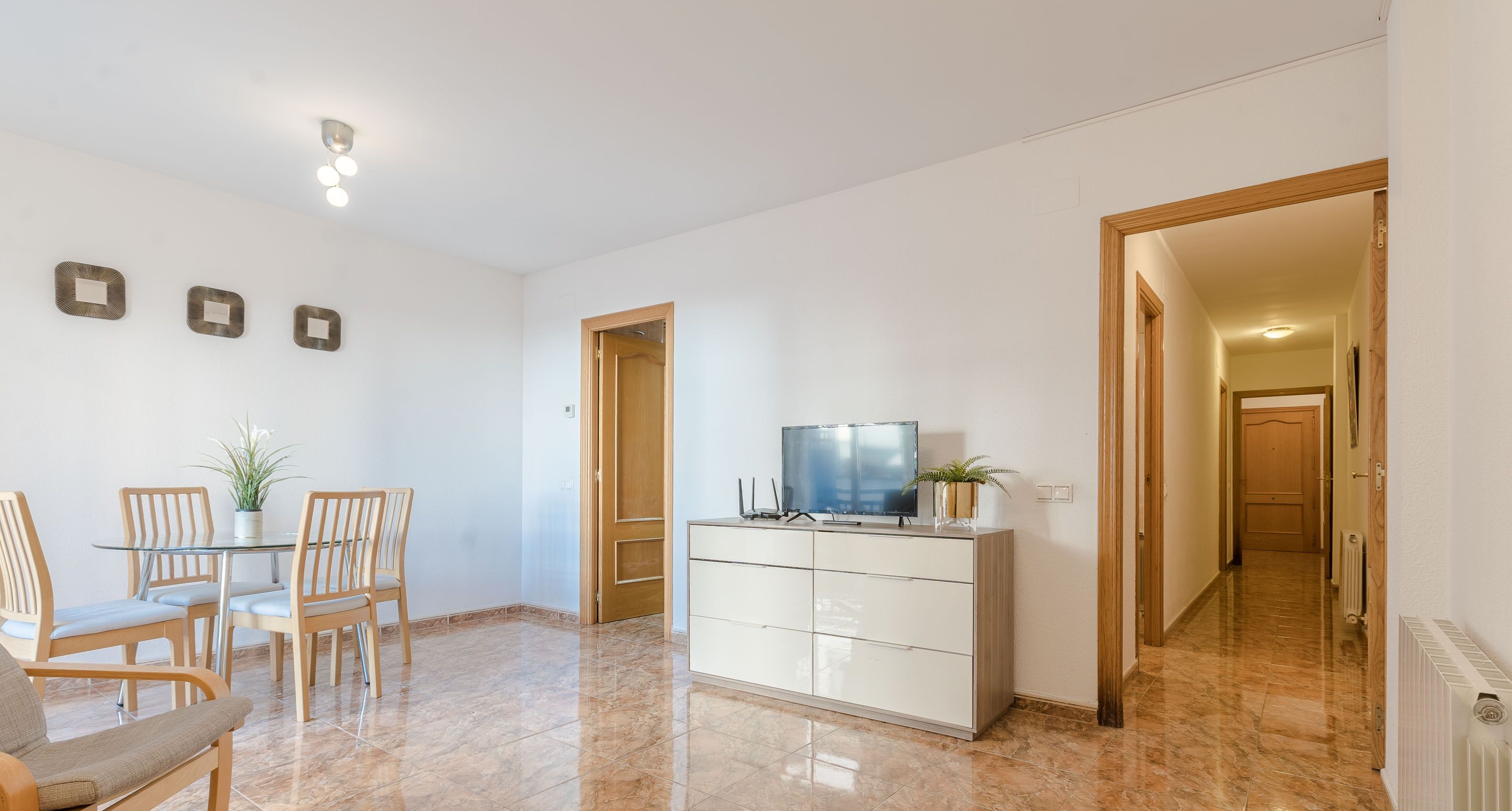 A spacious living area with a dining table, chairs, a TV, and a cabinet.