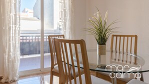 Un coin repas avec une table en verre, deux chaises en bois, une plante en pot et une porte-fenêtre coulissante donnant sur un balcon extérieur.