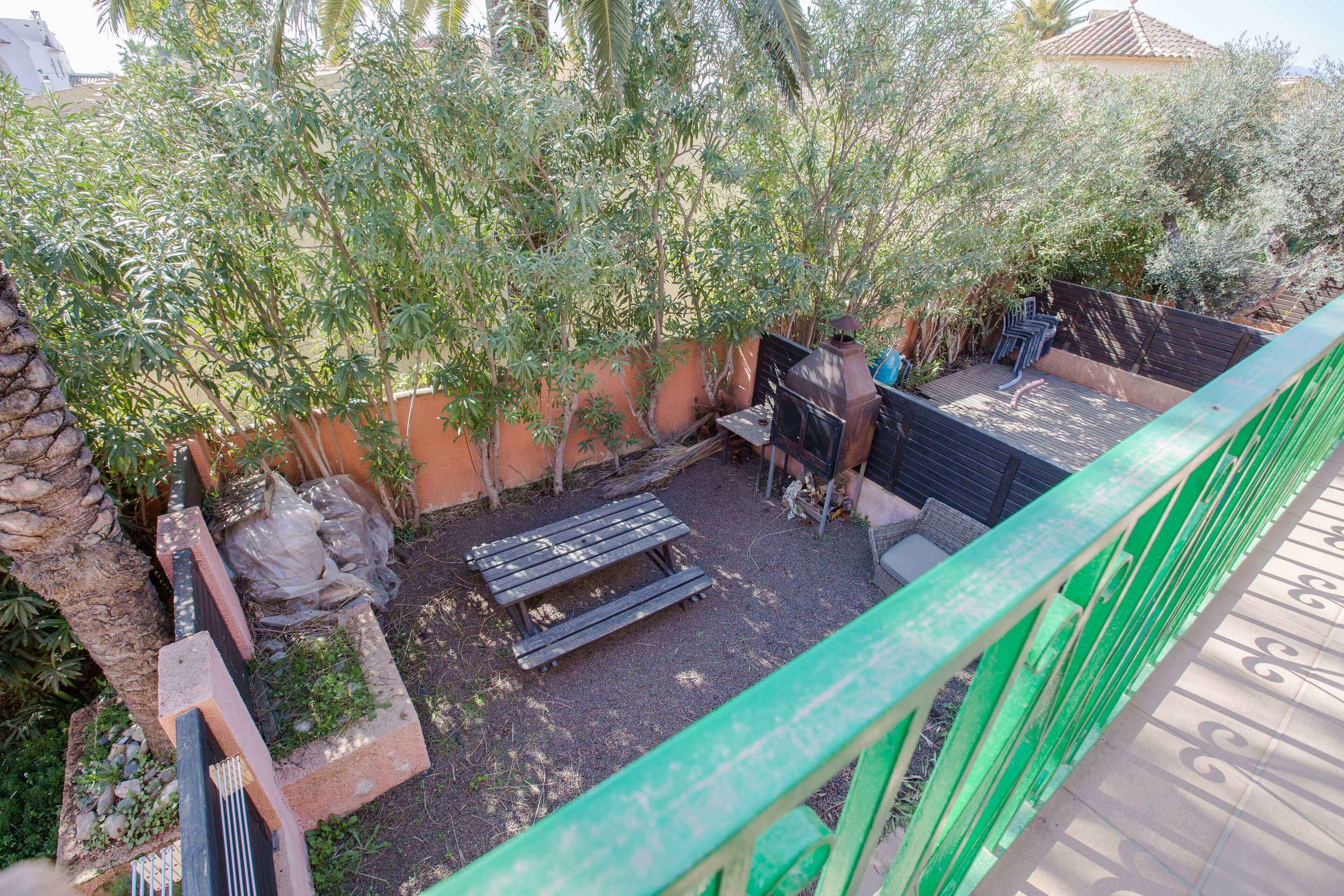 Un espace patio avec un banc en bois, une petite table et une rambarde verte.