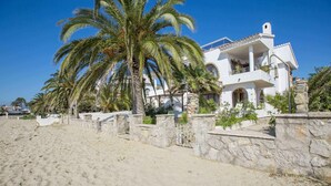 Une villa blanche avec un mur en pierre et des palmiers devant.