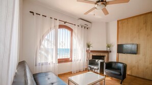 Un salon avec un canapé en cuir noir, une table basse blanche, une cheminée, un téléviseur fixé au mur et une vue sur la mer par une grande fenêtre.