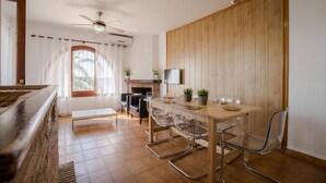 Un salon moderne avec une table à manger en bois, des chaises en verre transparent, une cheminée et un ventilateur de plafond.