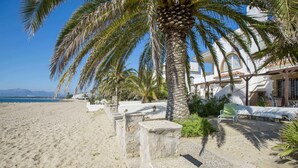 Une plage bordée de palmiers, un sentier pavé de pierres et un bâtiment à la façade blanche.