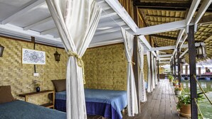 A wooden deck with two beds, each with a canopy, and a woven wall.