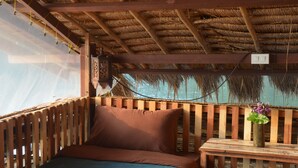 A wooden bed with a blue bedspread, a wooden nightstand with a vase of flowers, and a thatched roof.