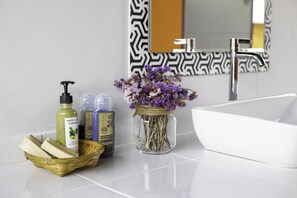 A bathroom with a white sink, a mirror with a black and white pattern, and a vase with purple flowers. There are also bottles of hair products and a basket with soap bars. - Houseboat Floating, Enjoy the sounds of nature whit a unique place. (Tambon Ban Pao)